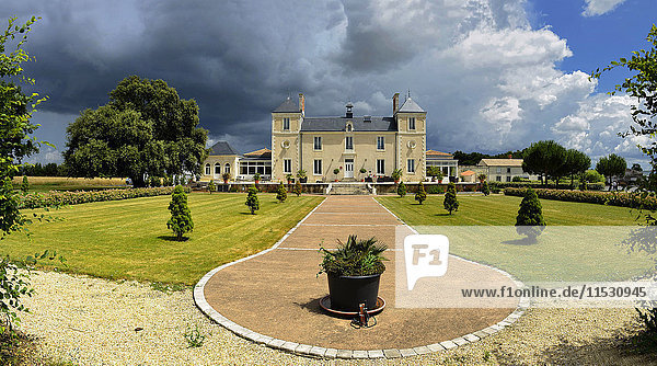 Frankreich  Vendee  Le Gue-de-Velluire  Schlosshotel Sebrandiere. Zwei quadratische Türme  Vorgarten  ein Mittelgang mit Sträuchern  links ein hundertjähriger Baum. Sturmwolken und blauer Himmel