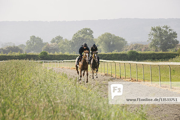 Two horses and riders on a gallops path  racing against each other in a training exercise. Racehorse training.