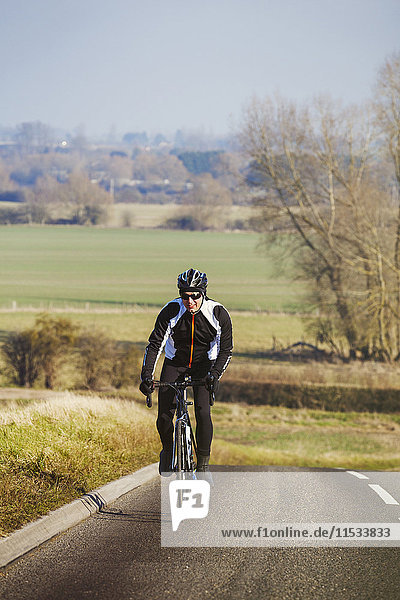 A man pedalling out of the saddle on a road bike  climbing up a hill. Front view.