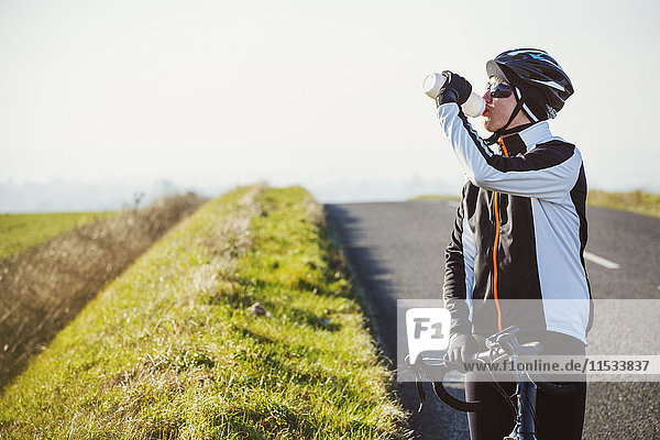 Ein Radfahrer am Straßenrand  der eine Pause macht und aus seiner Wasserflasche trinkt.