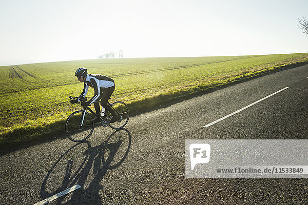 A cyclist riding along a country road on a clear sunny winter day. Shadow on the road surface.