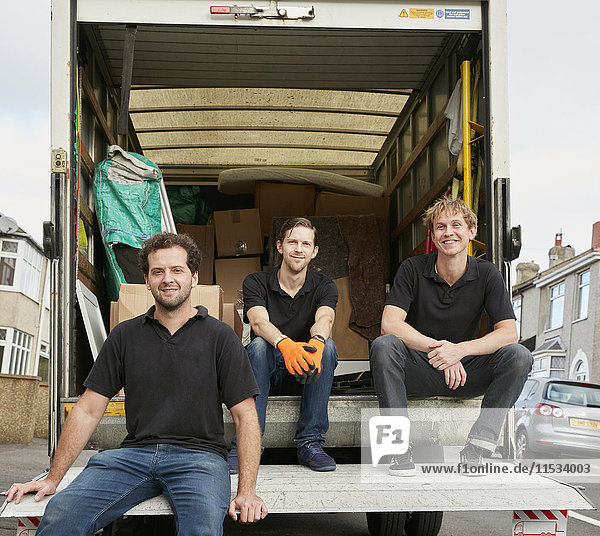 Umzugsunternehmen. Drei Männer in schwarzen Hemden  die hinten in ihrem Umzugswagen sitzen und eine Pause machen.
