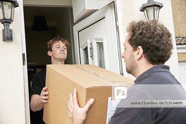 Umzugsunternehmen. Zwei Männer  die einen gepackten Karton aus einem Haus heben und tragen.