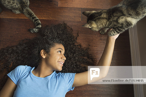 Ein auf dem Rücken liegendes Mädchen streichelt eine Katze.