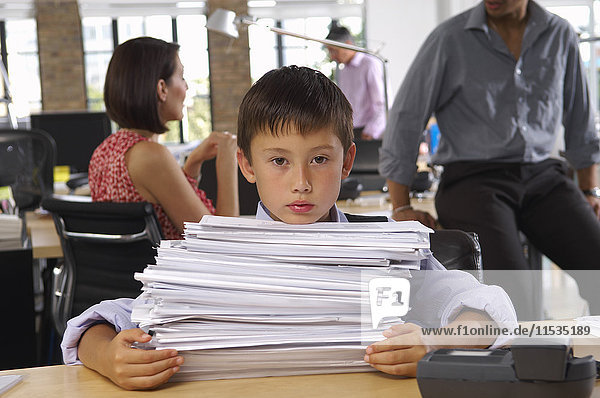 Junge im Büro mit Stapel von Papierkram