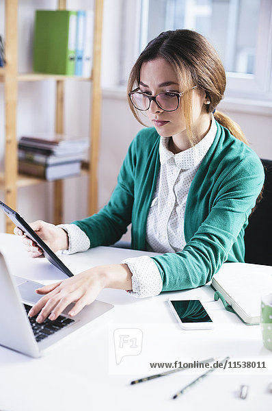 Junge Geschäftsfrau bei der Arbeit mit Laptop und digitalem Tablett im Büro