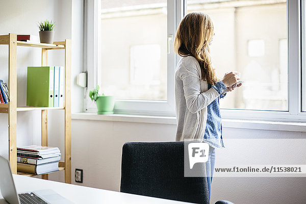 Junge Frau ruht sich bei einer Tasse Kaffee in ihrem Heimbüro aus.