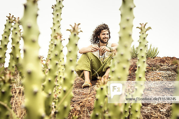 Man sitting on rock behind cacti  smiling