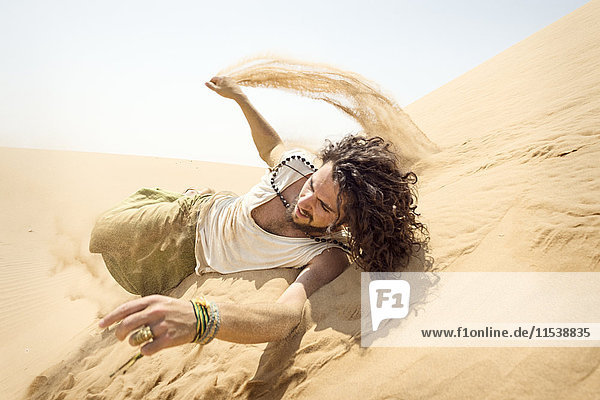 Man rolling down sand dune