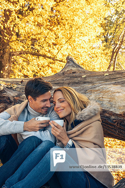 Lächelndes Paar mit Tassen im Herbstwald
