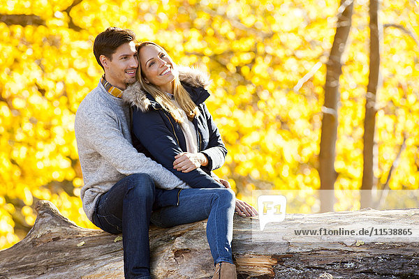 Happy couple enjoying autumn in a forest sitting on a trunk