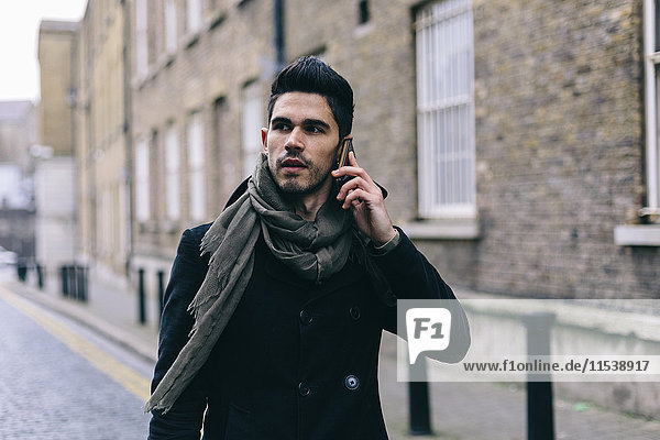 Young casual businessman walking in the street using mobile phone
