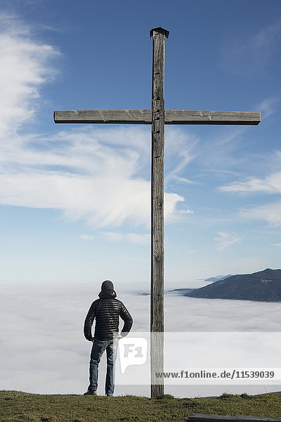 Deutschland  Bayern  Mann am Gipfelkreuz am Blomberg bei atmosphärischer Inversion
