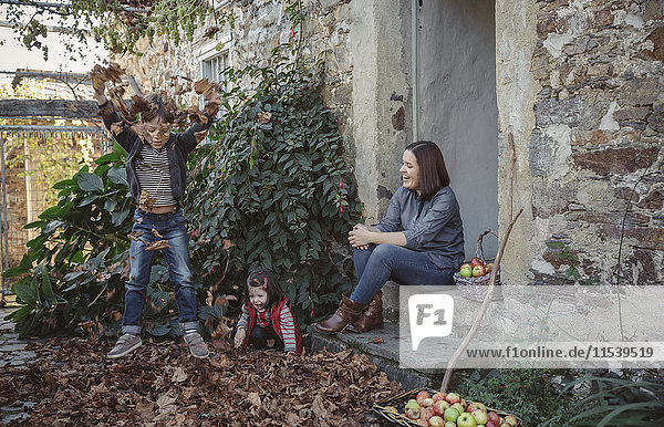 Spanien  Asturien  Frau sitzt am Eingang des Landhauses und beobachtet ihre Kinder beim Spielen mit Herbstlaub.