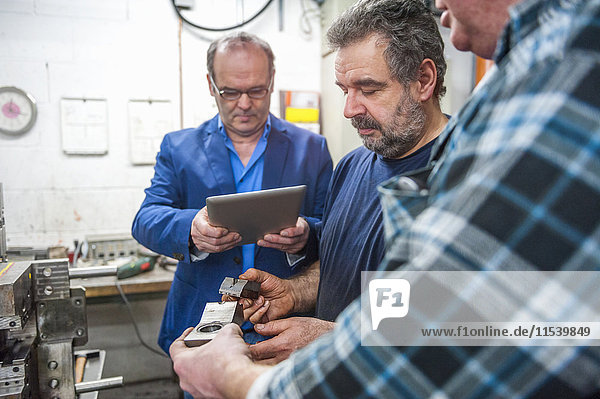 Drei Männer mit digitalem Tablett untersuchen Werkstücke