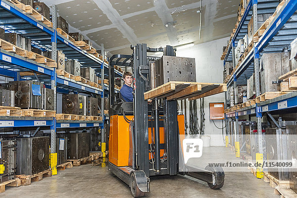 Warehouse worker driving forklift in storage for machine blocks