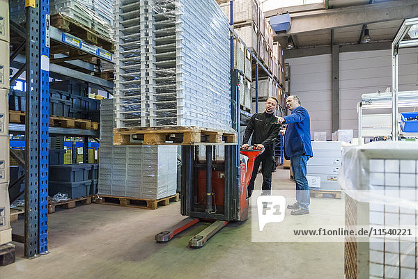Worker in warehouse transporting goods on forklift