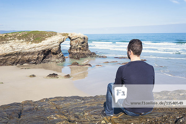 Spain  Ribadeo  back view of man sitting on rocks of Playa de Las Catedrales
