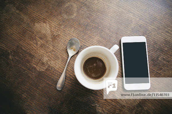 Kaffeetasse mit Kaffeeresten  Löffel und Smartphone auf Holz