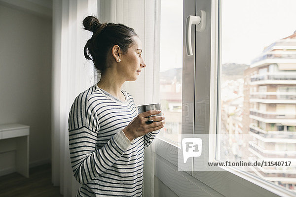 Frau hält eine Tasse Kaffee und schaut aus dem Fenster.