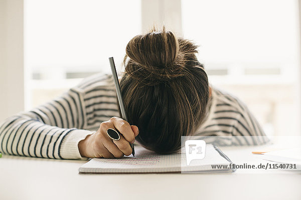 Frau schreibt auf Notizblock und legt ihren Kopf auf den Tisch.
