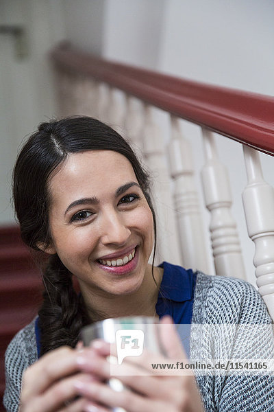 Porträt einer lächelnden Frau im Treppenhaus mit einer Tasse Kaffee
