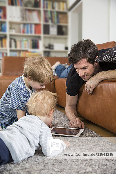 Vater liegt mit seinen Söhnen auf dem Sofa und benutzt ein digitales Tablett.
