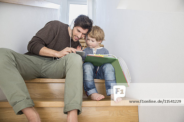 Vater und Sohn sitzen auf der Treppe  lesen Buch und Musik hören