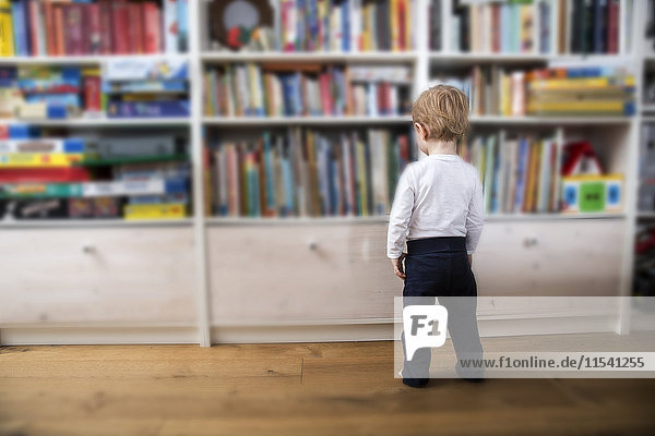 Kleiner Junge steht vor dem Bücherregal