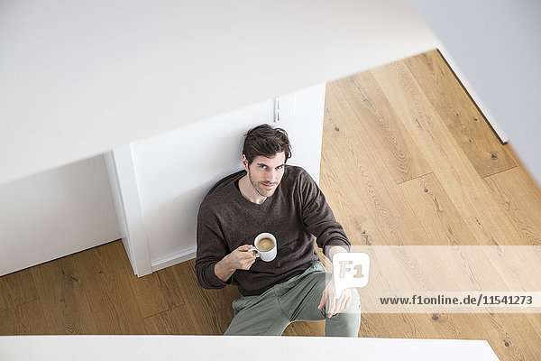 Mann sitzt auf dem Boden und trinkt Kaffee.