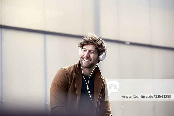 Smiling young man listening music with headphones at backlight