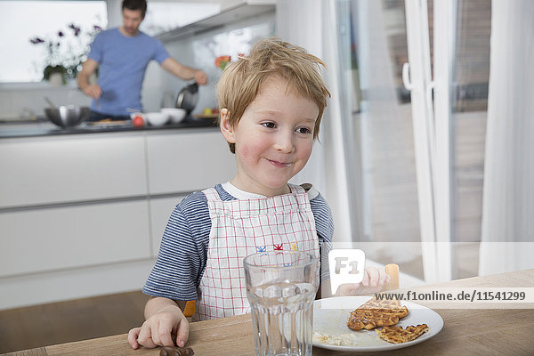 Kleiner Junge isst Waffeln in der Küche