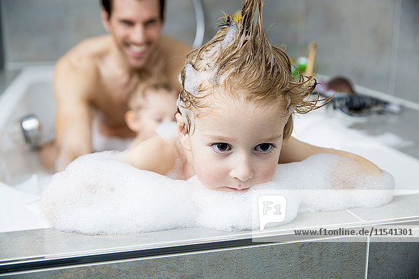 Boy looking pensive with father and brother in bathtub