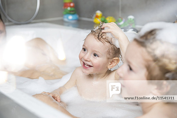 Little boy having fun in bathtub with brother and father
