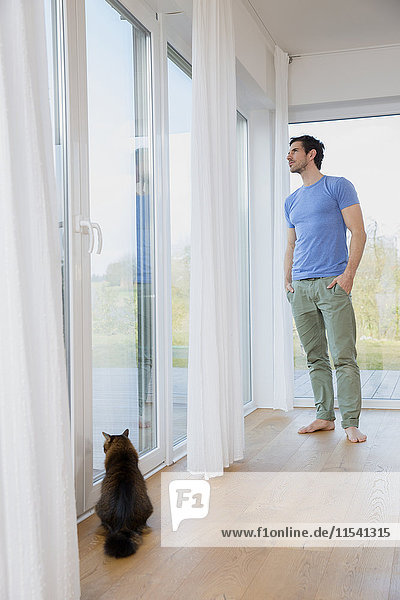 Mann zu Hause am Fenster stehend mit Blick nach draußen