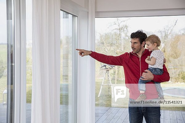 Vater hält den Sohn in den Armen und zeigt aus dem Fenster.