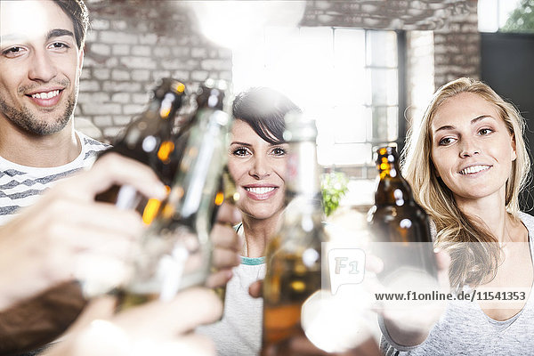 Friends clinking beer bottles in kitchen