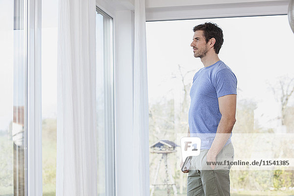 Man at home standing at window looking out