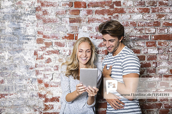 Fröhliches junges Paar schaut gemeinsam auf das digitale Tablett