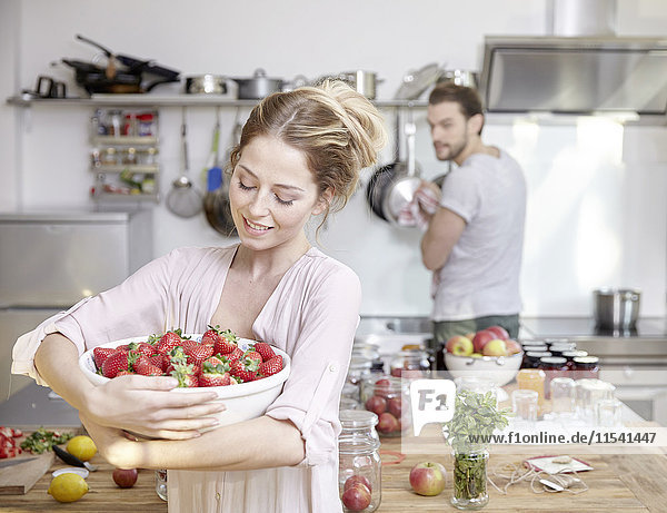Young woman holding bowl with strawberries in kitchen