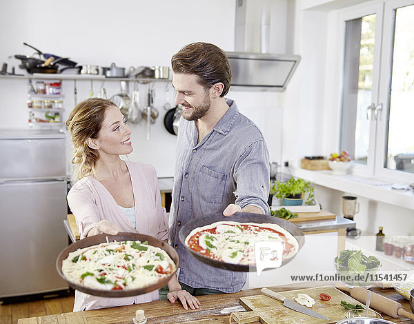 Paar Backformen mit rohen Pizzen in der Küche