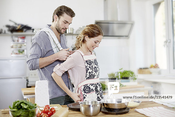 Man helping woman putting on apron in kitchen