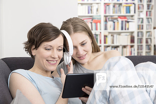 Mutter und erwachsene Tochter mit gemeinsamem digitalen Tablett und Kopfhörer