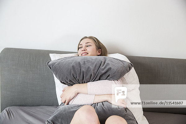 Happy young woman lying on her bed hugging pillow