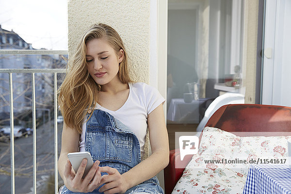 Porträt einer jungen Frau auf dem Balkon mit Blick auf ihr Smartphone