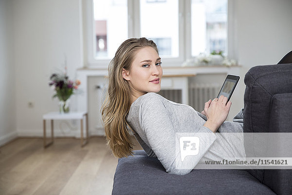 Porträt einer jungen Frau auf der Couch liegend mit digitalem Tablett