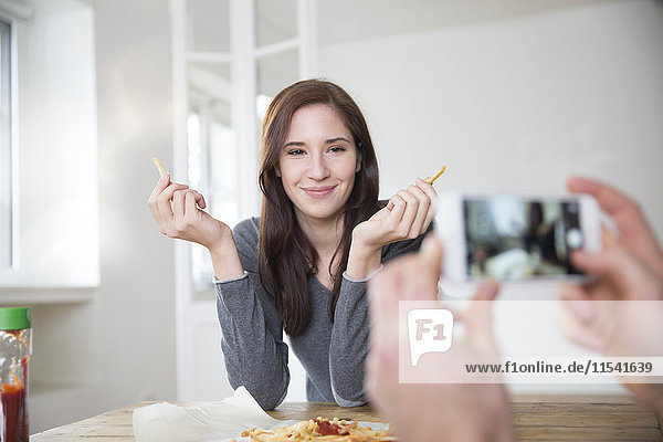 Junger Mann beim Fotografieren seiner lächelnden Freundin mit Pommes frites