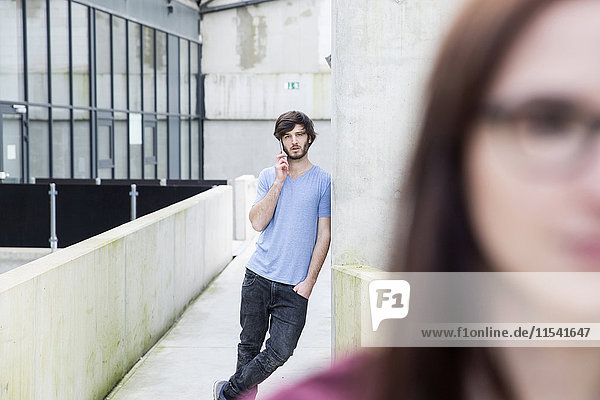 Young man leaning against concrete wall telephoning with smartphone