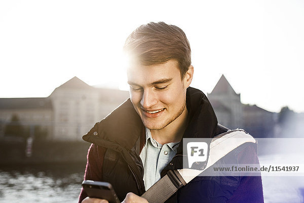 Germany  Berlin  young man holding smartphone at River Spree