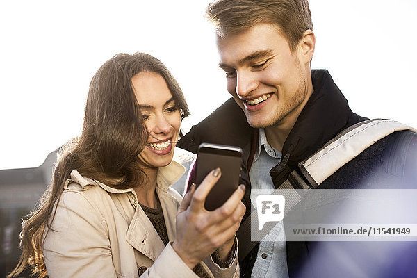 Lächelndes junges Paar schaut auf das Smartphone im Freien
